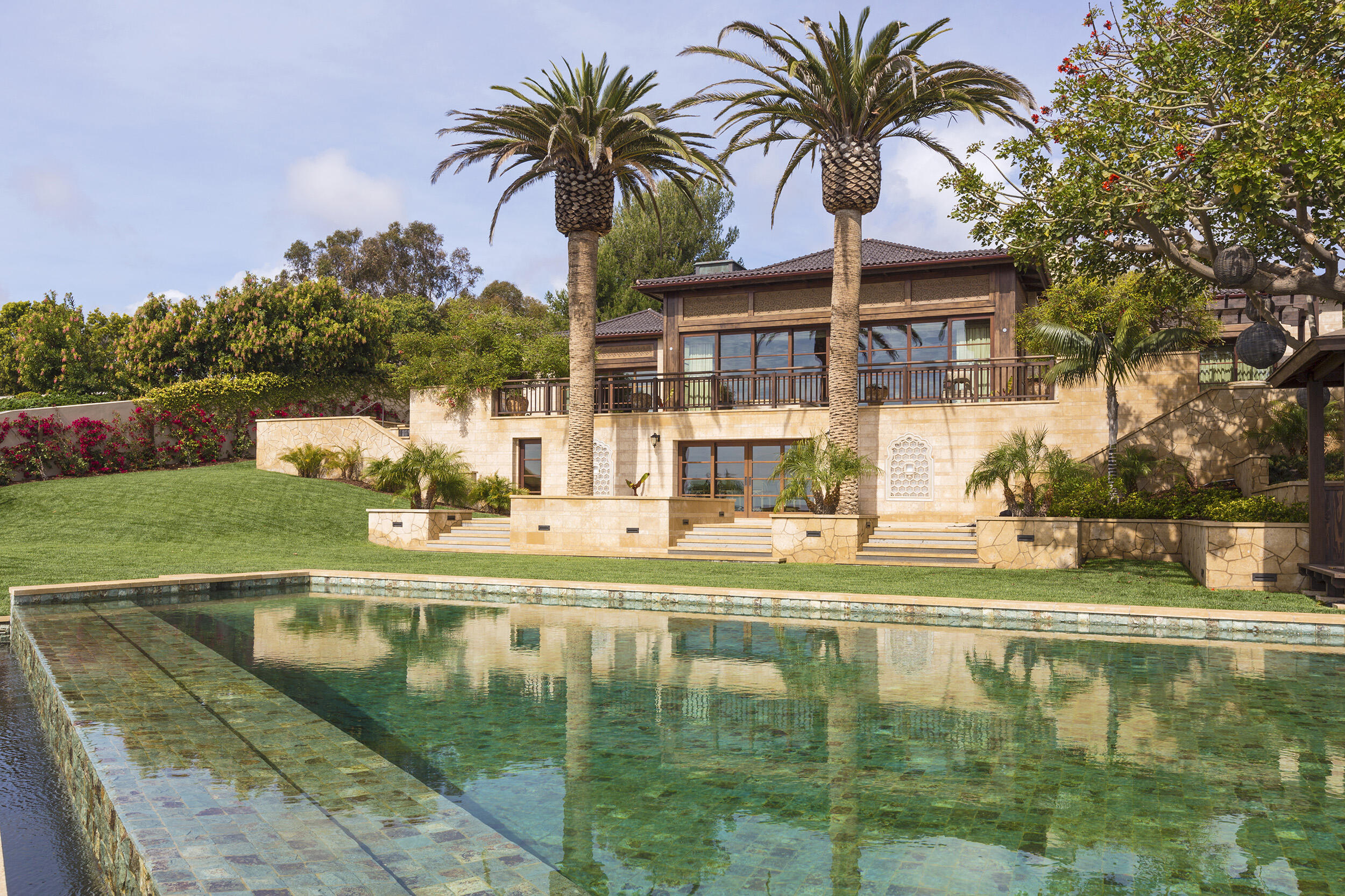 Rear Facade of a Malibu Residence featuring infinity-edge pool, natural stone cladding and clay tile roof by Hayne Architects.